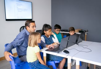 Instructor guiding kids in a small group tech class with laptops