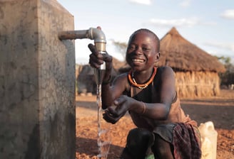 Smiling child drinking clean water from a well in a rural African village