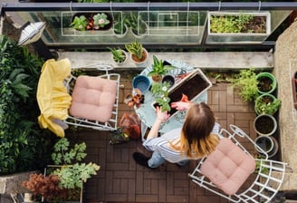 a woman sitting at a table with a phone in green balcony with plants and natures