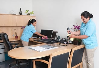 two women in blue shirts cleaning a desk