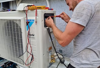 a man in a gray shirt is working on a white air conditioner