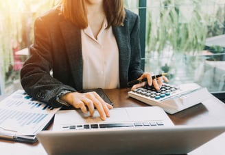 an accountant sitting at a desk with a calculator and laptop reviewing management reports