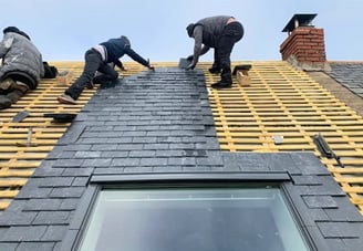 Trois couvreurs posant des ardoises sur charpente de toiture avec Velux