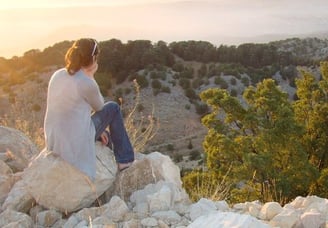 a woman sitting on a rock wall with a view of the mountains