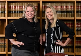 two women standing in front of a bookcase in an office