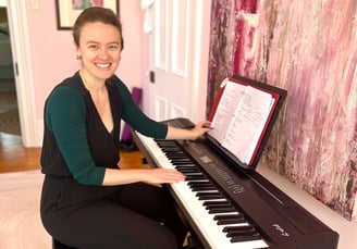 Ellen, a white woman, sits at the piano and smiles at the camera