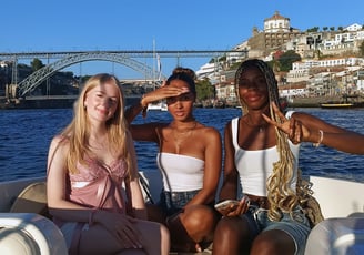 Three girls posing for a photo on the Endure speedboat with Dom Luís I Bridge in the background