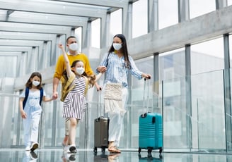 a family of four wearing masks and masks on their faces and travel bag