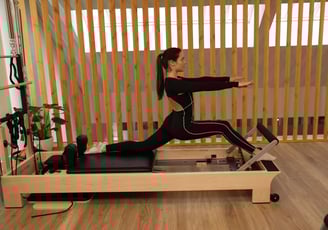 Woman performing a advanced split stretch on a Pilates reformer in a modern studio.