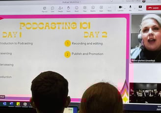 A classroom of students looking at a big screen with text saying Podcasting 101