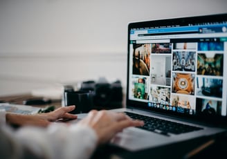 a person is typing in his laptop which displays some contents and posters