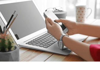 Enquadramento de uma pessoa olhando um celular frente à um notebook