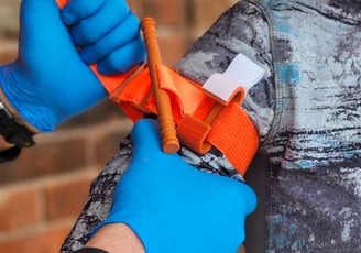 C.A.T. 7, tourniquet being applied to arm during training using two hands wearing blue nitrile glove