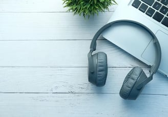 a laptop and headphones on a desk with a plant in the background, working on a transcription