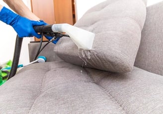 Professional upholstery cleaner using an extraction machine to deep clean a couch, expert care.