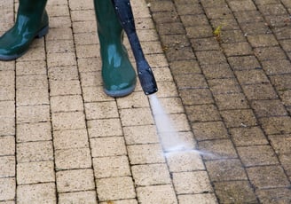 Man using a power washer on a surface, demonstrating before & after, with a visibly clean area.