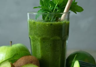 Copo de suco verde com folhas de hortelã, rodeado de ingredientes naturais como kiwi, pepino, maçã