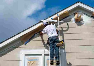 a man on a ladder painting a house with a sprayer