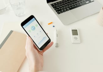 Person holding a Glucose monitor reader at a computer desk