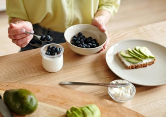 Person eating blueberries, yoghurt, avocado on toast