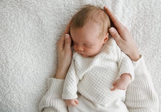 a newborn baby photoshoot. The baby is sleeping on a blanket. mum holding the baby in her hands