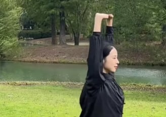a woman in a black jacket and jeans standing in a park