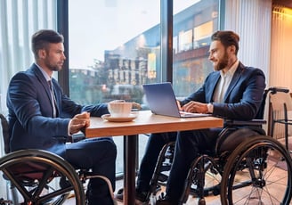 Zwei Rollstuhlfahrer sitzen für ein Beratungsgespräch in einem Café