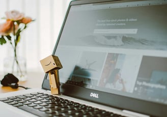 computador aberto com clip segurando uma caixa com logo amazon um vaso de flores amarelas ao fundo