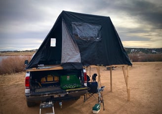 A truck with a cookstove on it's tailgate, cargo in it's bed, and a fold-out tent on it's bed
