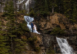 Bride and groom standing on a cliff next to a waterfall in Banff