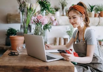 A small businesswoman ownwer sitting on her desk with her laptop and a mobile phone on her hand