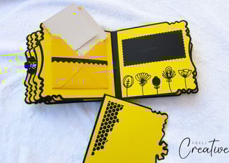 Yellow handmade scrapbook album with black floral and honeycomb designs. Open envelope holds white c