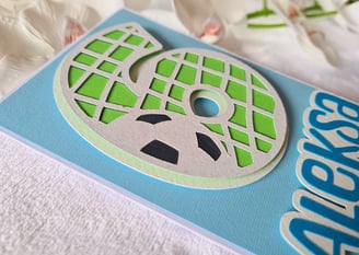 Greeting card with a textured number 6 cut-out of a stylized soccer ball in green and gray. Blue bac
