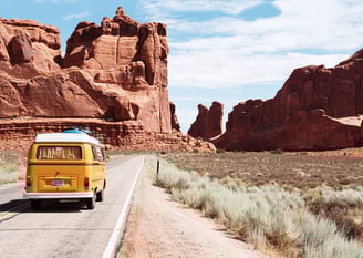 a yellow van driving down a road with moutain rocks in the background