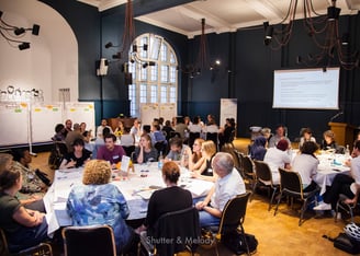 Mehrere runde Tische mit Workshop-Teilnehmern bei Refugio in Berlin.