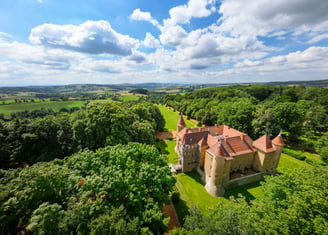 a castle like building with a large tower in the middle of a lush green field