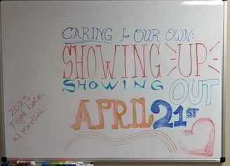 photo: whiteboard reads "CARING FOR OUR OWN: SHOWING UP, SHOWING OUT, APRIL 21ST; 2023 Fight back w/kindness"