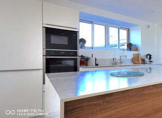 Cuisine blanche avec îlot en bois et plan de travail en marbre. Plaque de cuisson avec hotte intégré