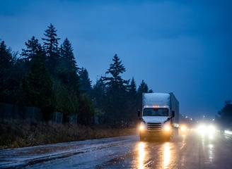 After-hours delivery truck driving at night on wet road — reliable freight service after hours.