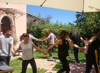 a group of people holding hands and dancing in a garden, classe di bioenergetica