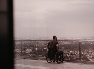 Mann mit Rollstuhl ist auf einem Hotel-Balkon und schaut über eine Stadt