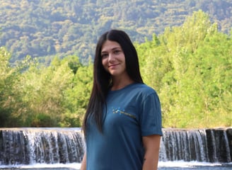 astrid mauri istruttrice certificata del metodo wim hof, davanti a una cascata con maglietta e logo 