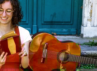 musicienne en train de lire un livre/a woman in a red dress reading on stairs with guitar beside her