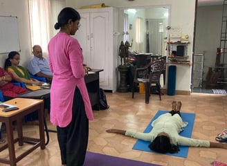 a woman in a pink shirt is standing in a room with several people during a teacher yoga class