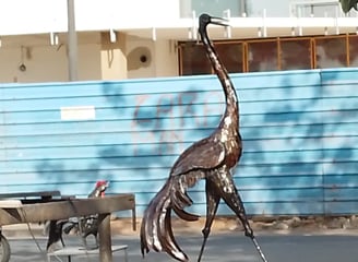 Sculpture grandeur nature d’une grue en métal recyclé, exposée sur un trottoir urbain à Dakar