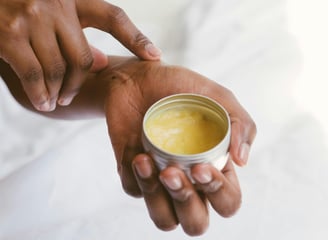 a person holding a cup of herbal salve in their hands