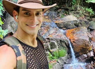 Travel writer Rick Silvia smiles at the camera wearing a cowboy hat in front of a waterfall