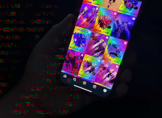 A hand holding a phone with an instagram layout on it showing different posts.
