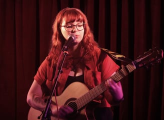 Moss.E performing on stage at an event with a guitar and microphone.