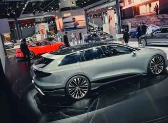A slick, modern exhibition space featuring several high-end cars. A white sedan is prominently displ